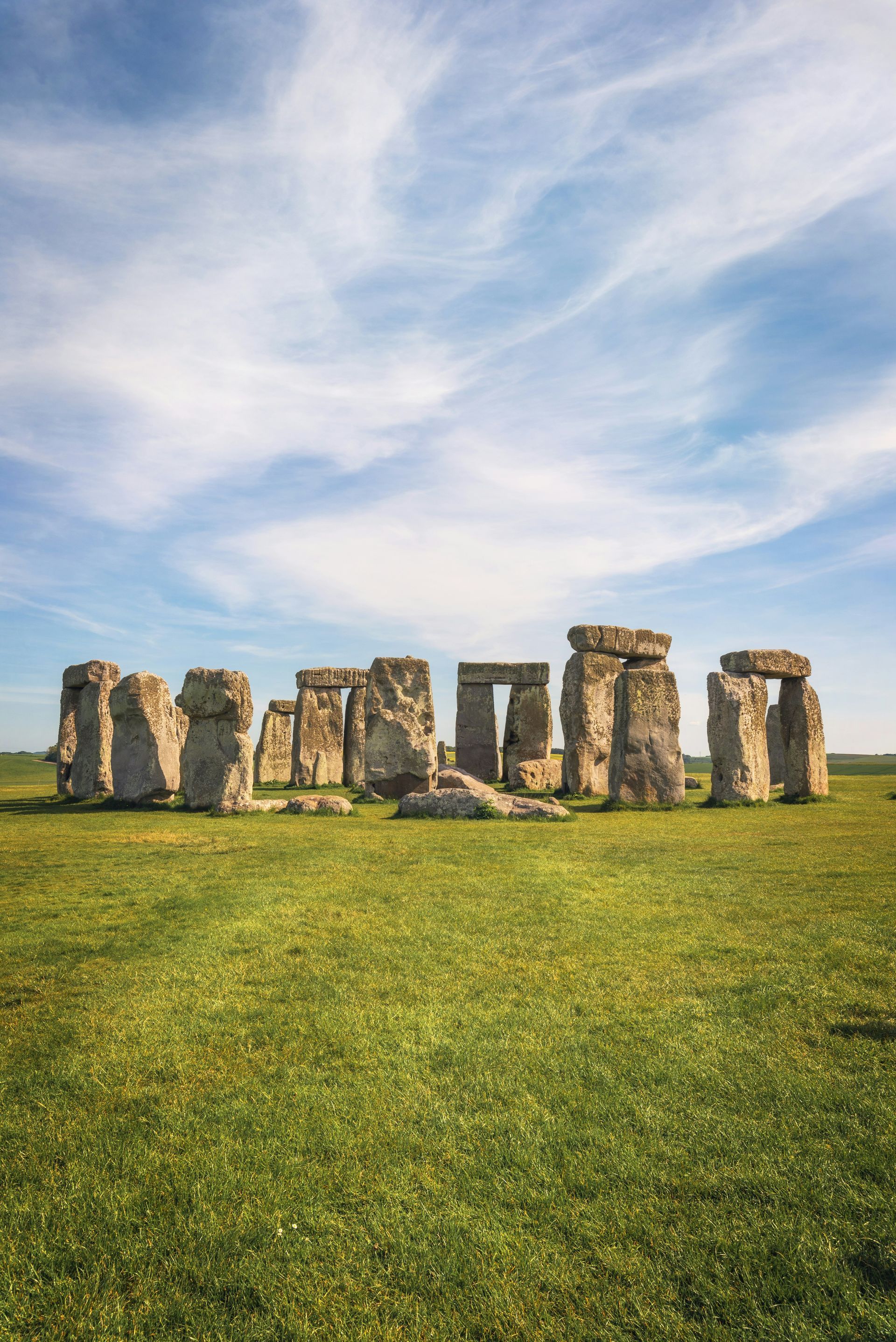 Stonehenge standing in a grassy field under a blue sky with wispy clouds