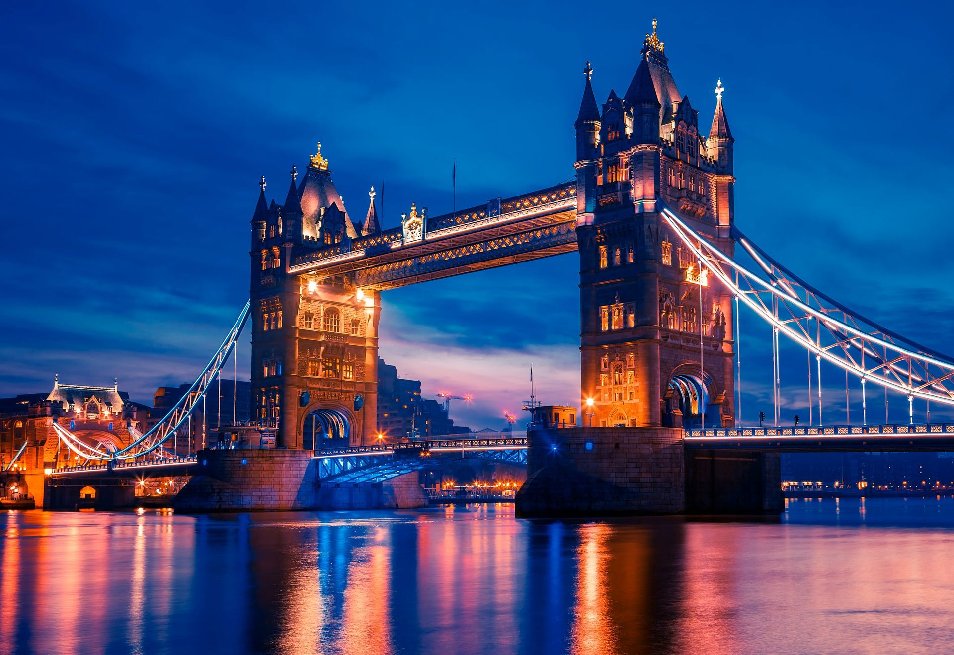 Tower Bridge lit at dusk over the River Thames, with reflections shimmering on the water.