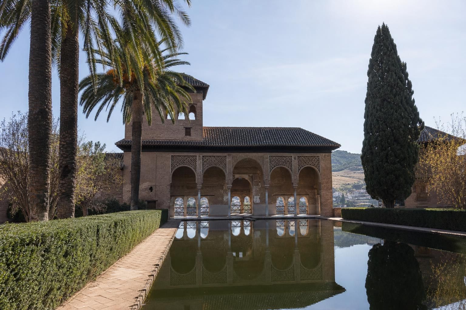 Historic stone courtyard with arched colonnade, reflecting pool, palm trees, and clear sky