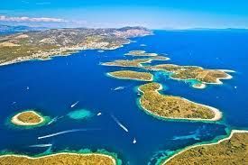 Azure sea with scattered islands, boat traffic, and coastal land under a clear blue sky.