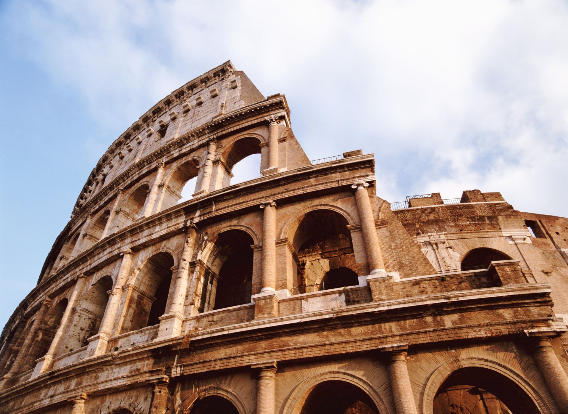 Colosseum in Rome, Italy, with arched windows and damaged exterior against a blue sky.