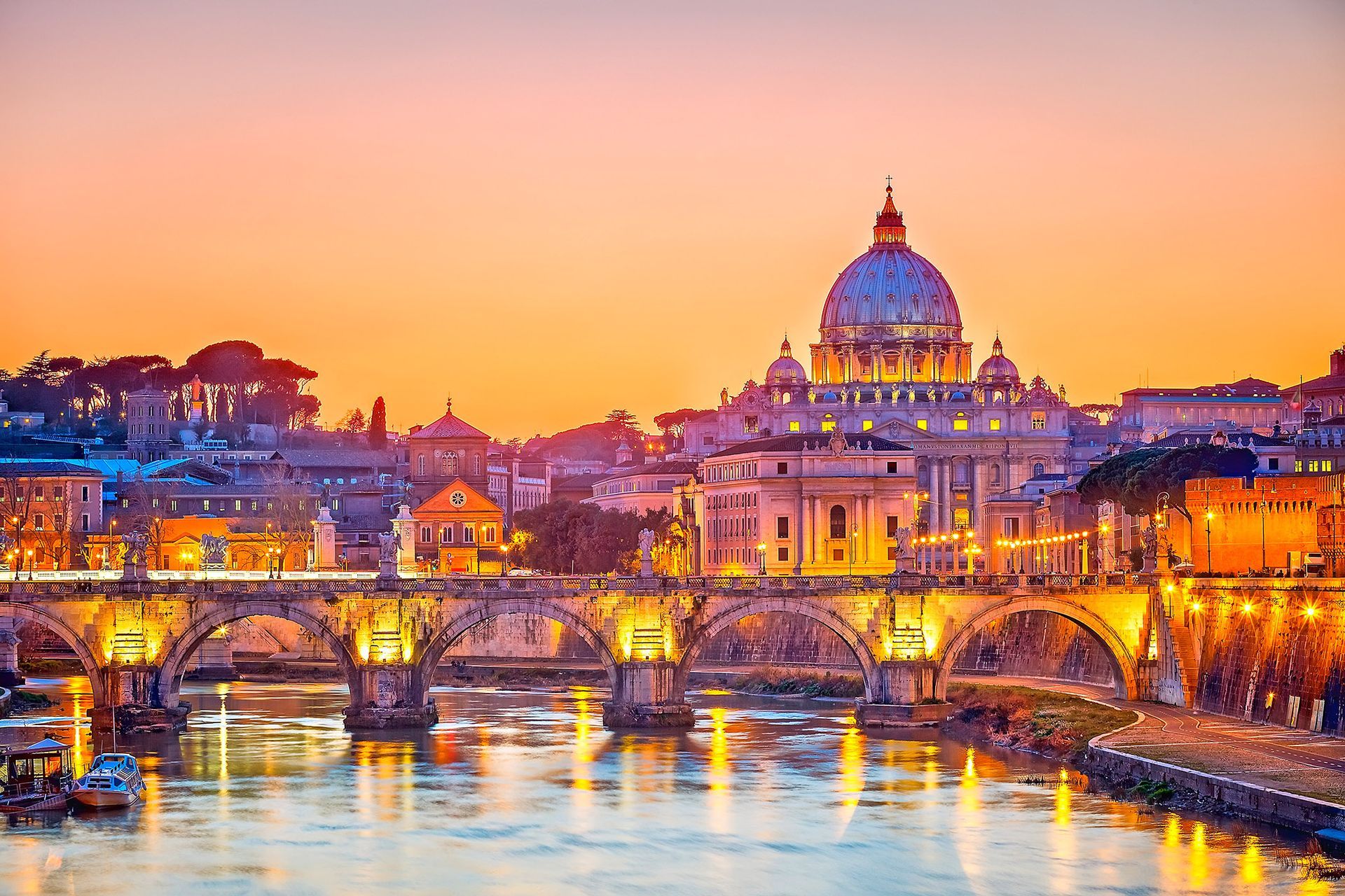Sunset over Rome, Italy, with St. Peter's Basilica dome lit up and the illuminated Ponte Sant'Angelo bridge.