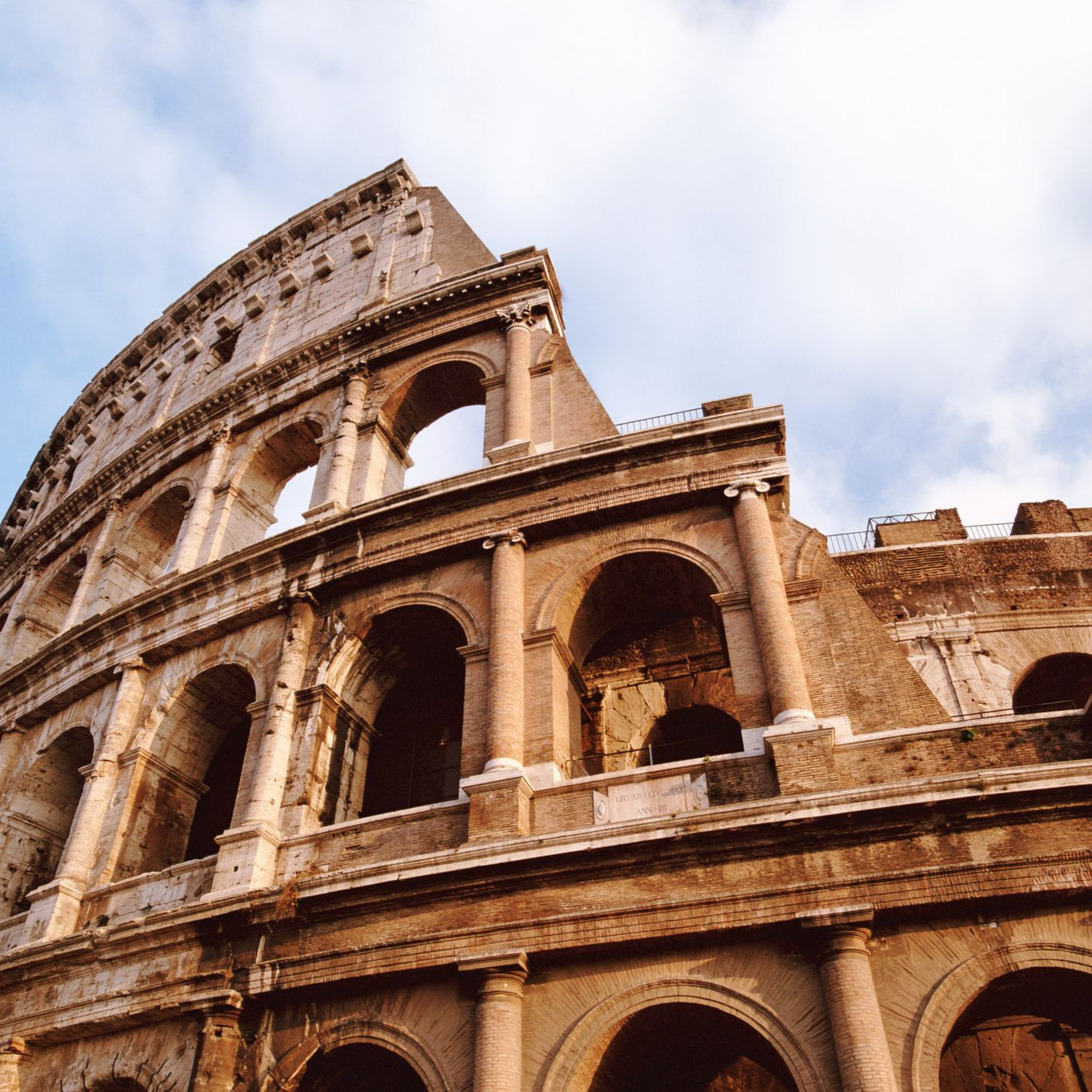 The Colosseum in Rome viewed from below against a blue sky.