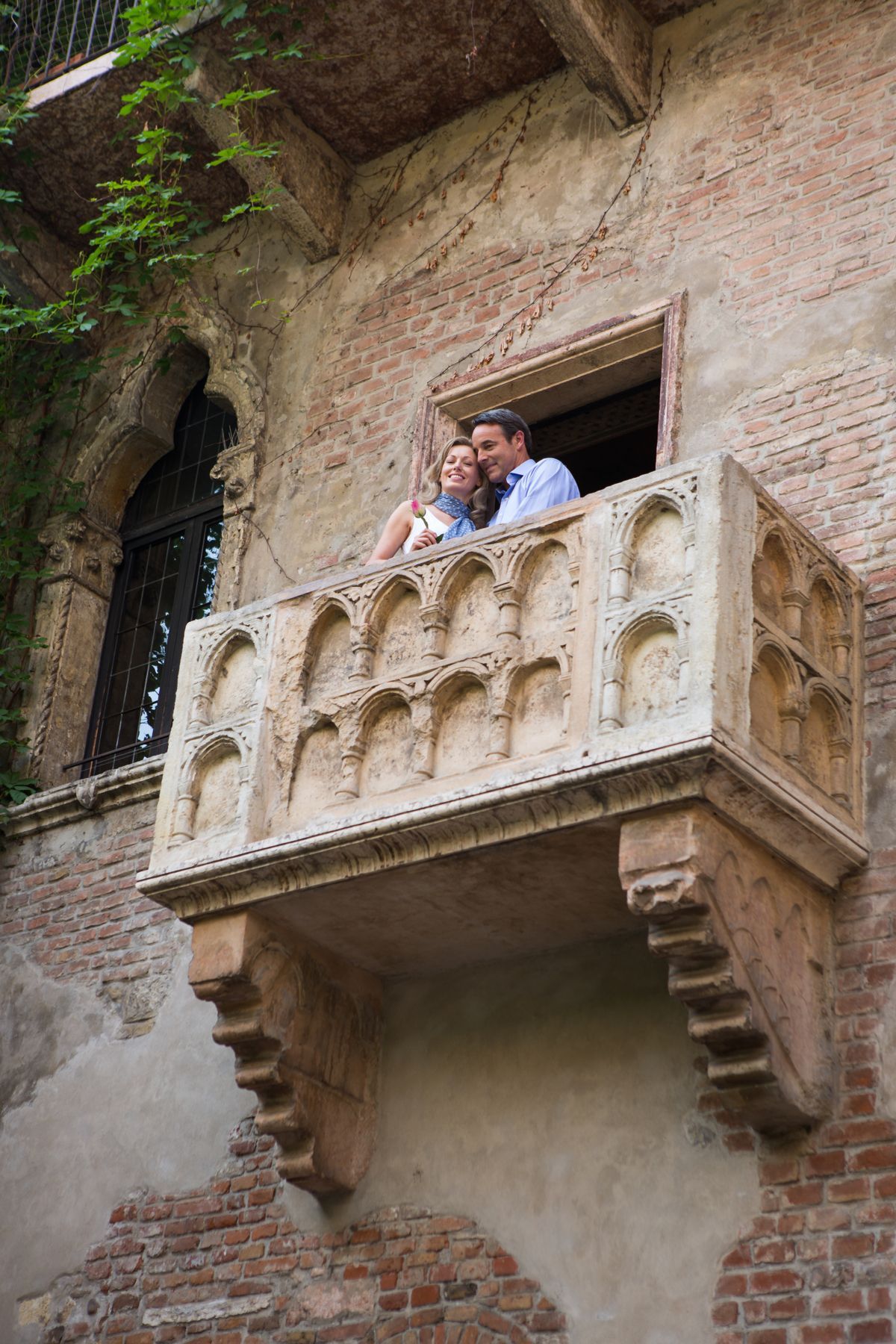 Couple leaning on ornate stone balcony in a historic building facade