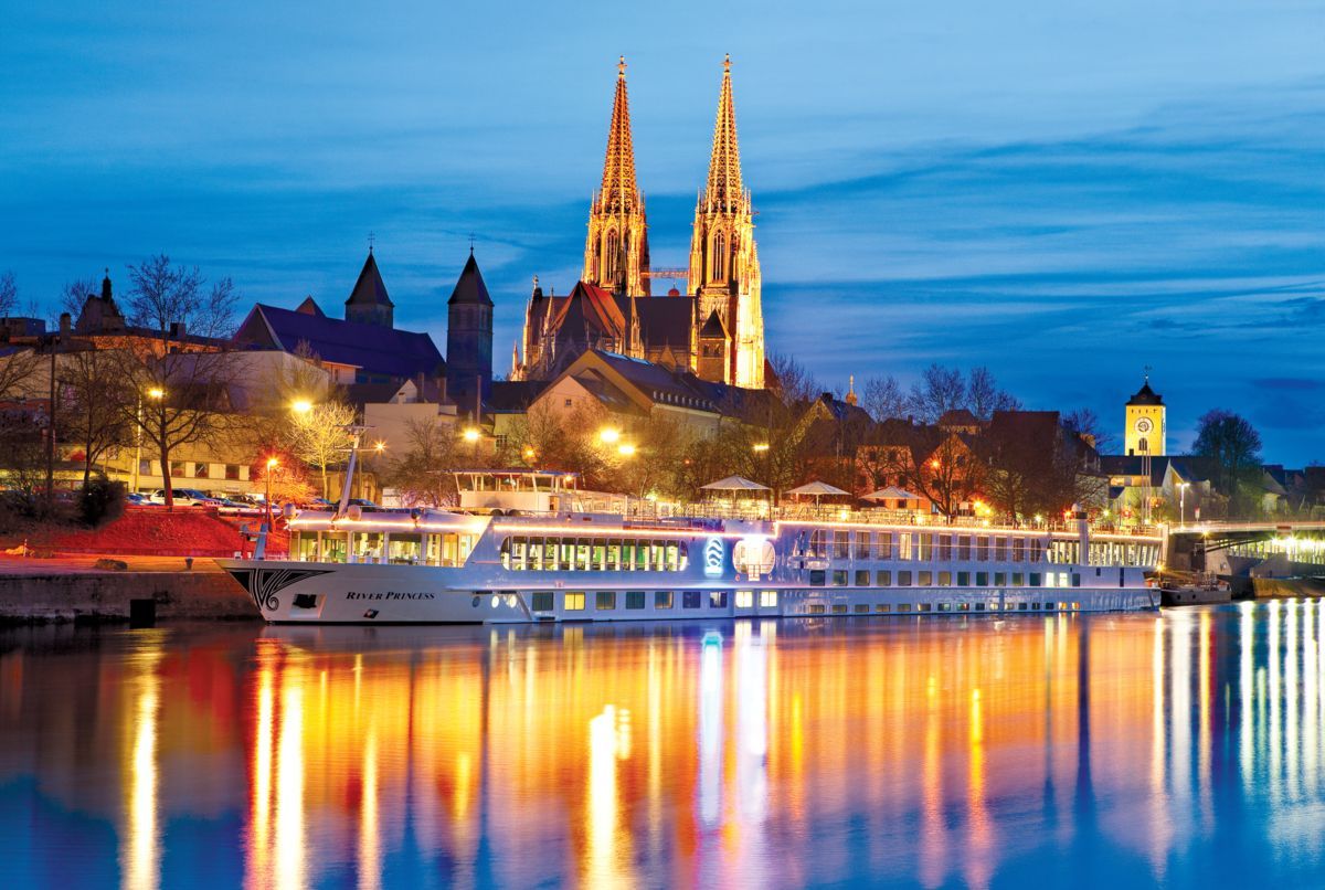Night river scene with illuminated cathedral, city lights, and a docked boat reflecting on the water