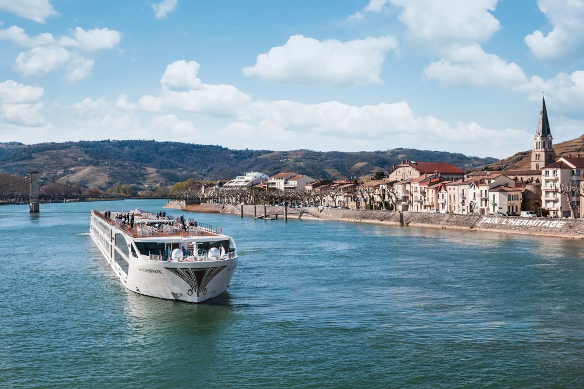 White river cruise boat on a blue river passing a town with a church spire and hills under a cloudy sky