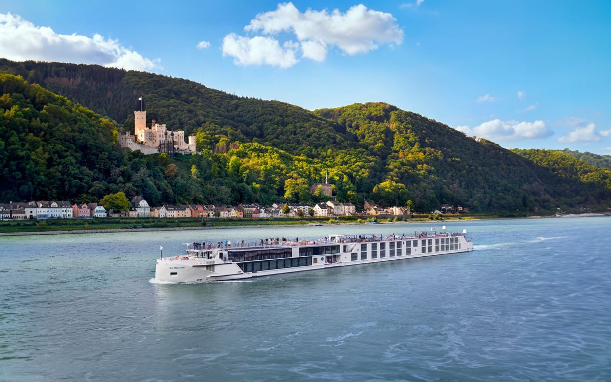 White river cruise boat on a wide blue river beside a green hillside and riverside town