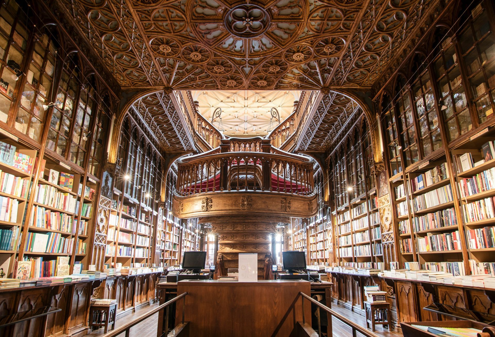 Grand ornate library interior with tall bookshelves, carved wooden ceiling, and a central balcony.