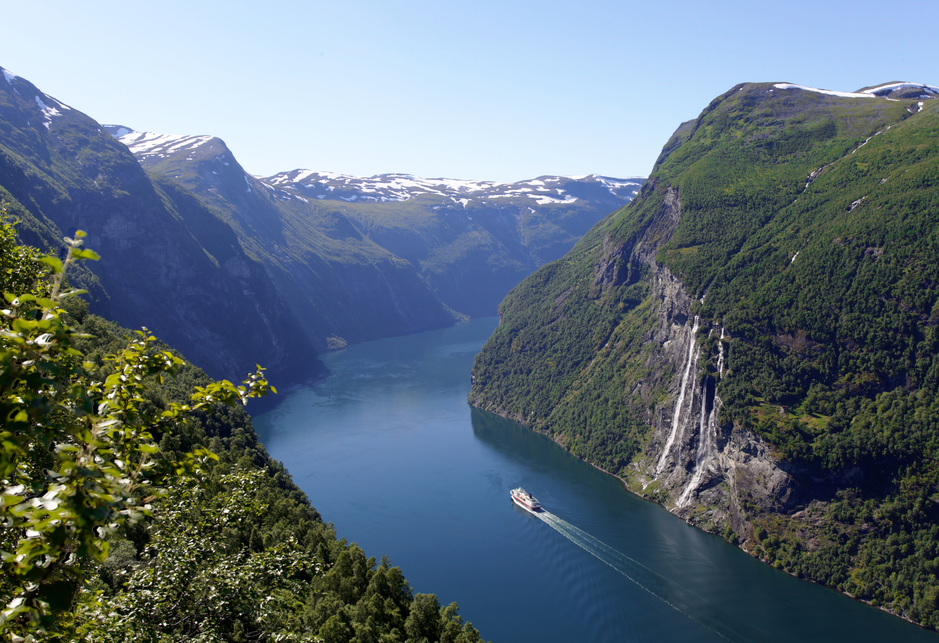 Mountain fjord with steep green cliffs and a boat on deep blue water under a clear sky