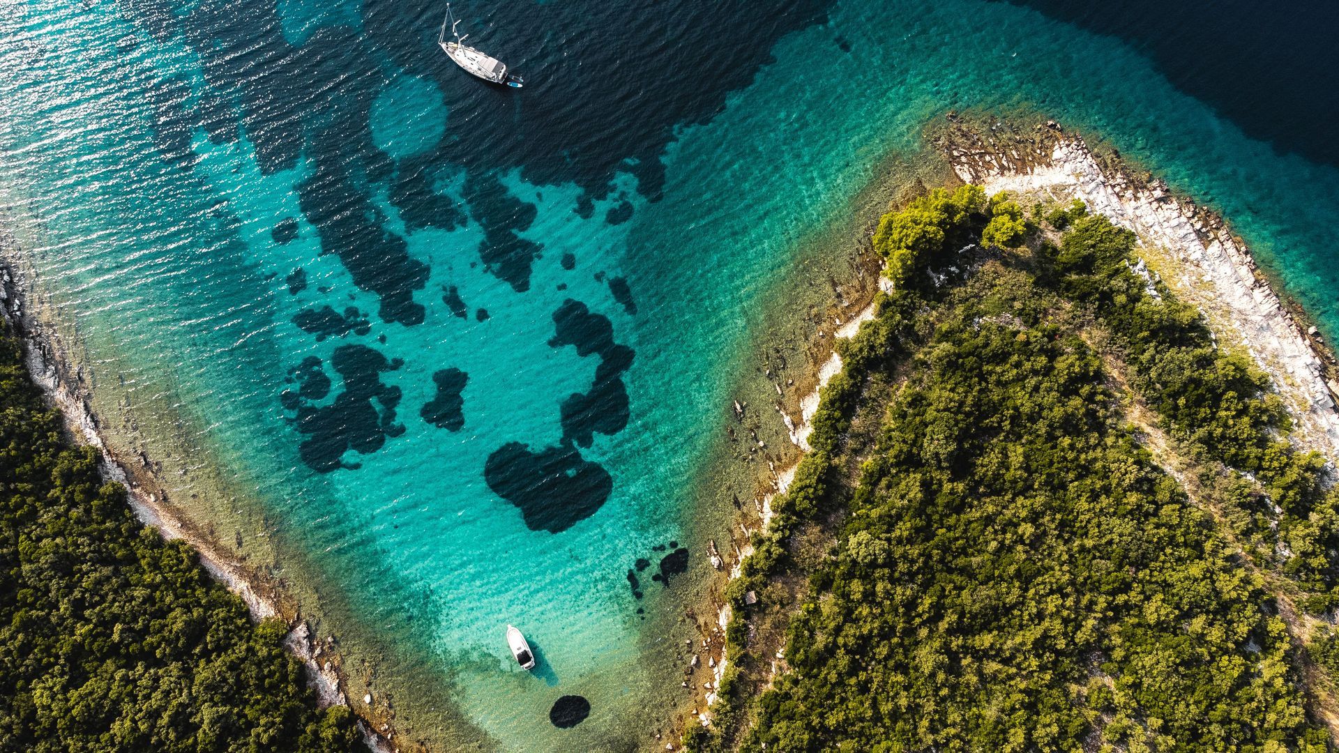 Aerial view of turquoise water beside a green, rocky coastal peninsula in Croatia