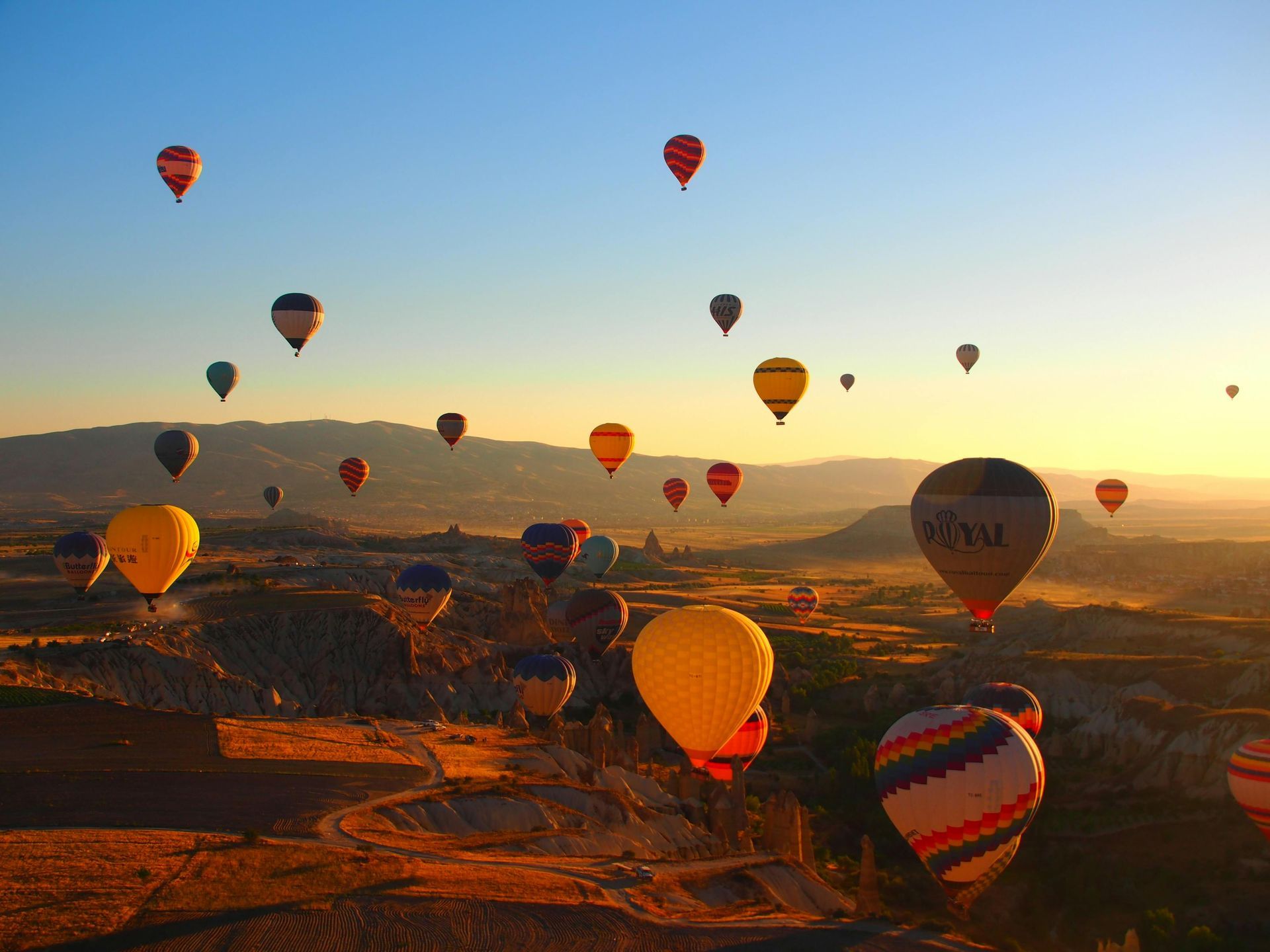 Hot air balloons over a valley at sunrise, with a clear blue sky.