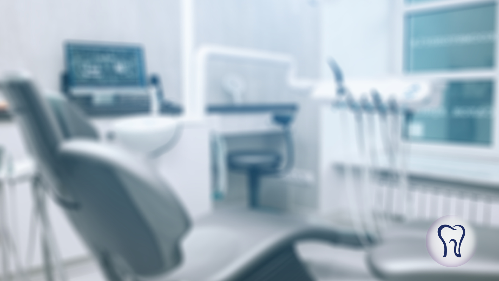 Blurred view of a dental office with chair, equipment, and monitor.