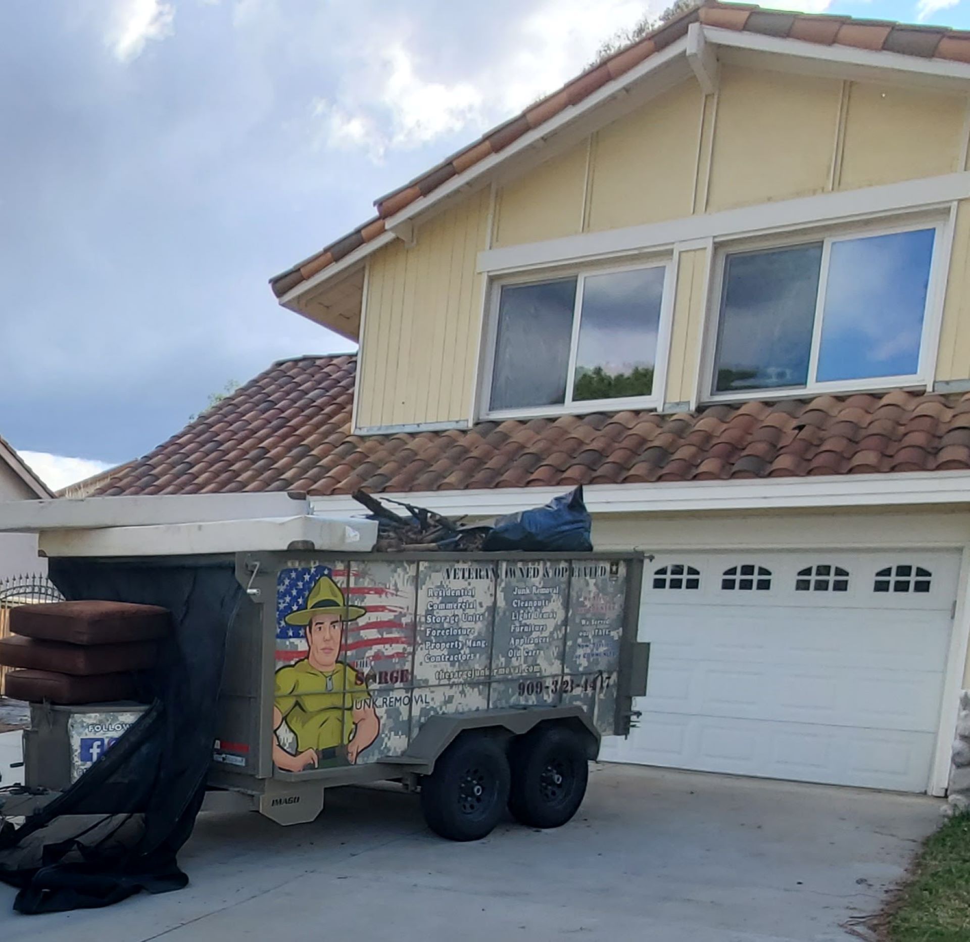 A trailer with a mural of a man in a hat and American flag, parked in front of a two-story house.