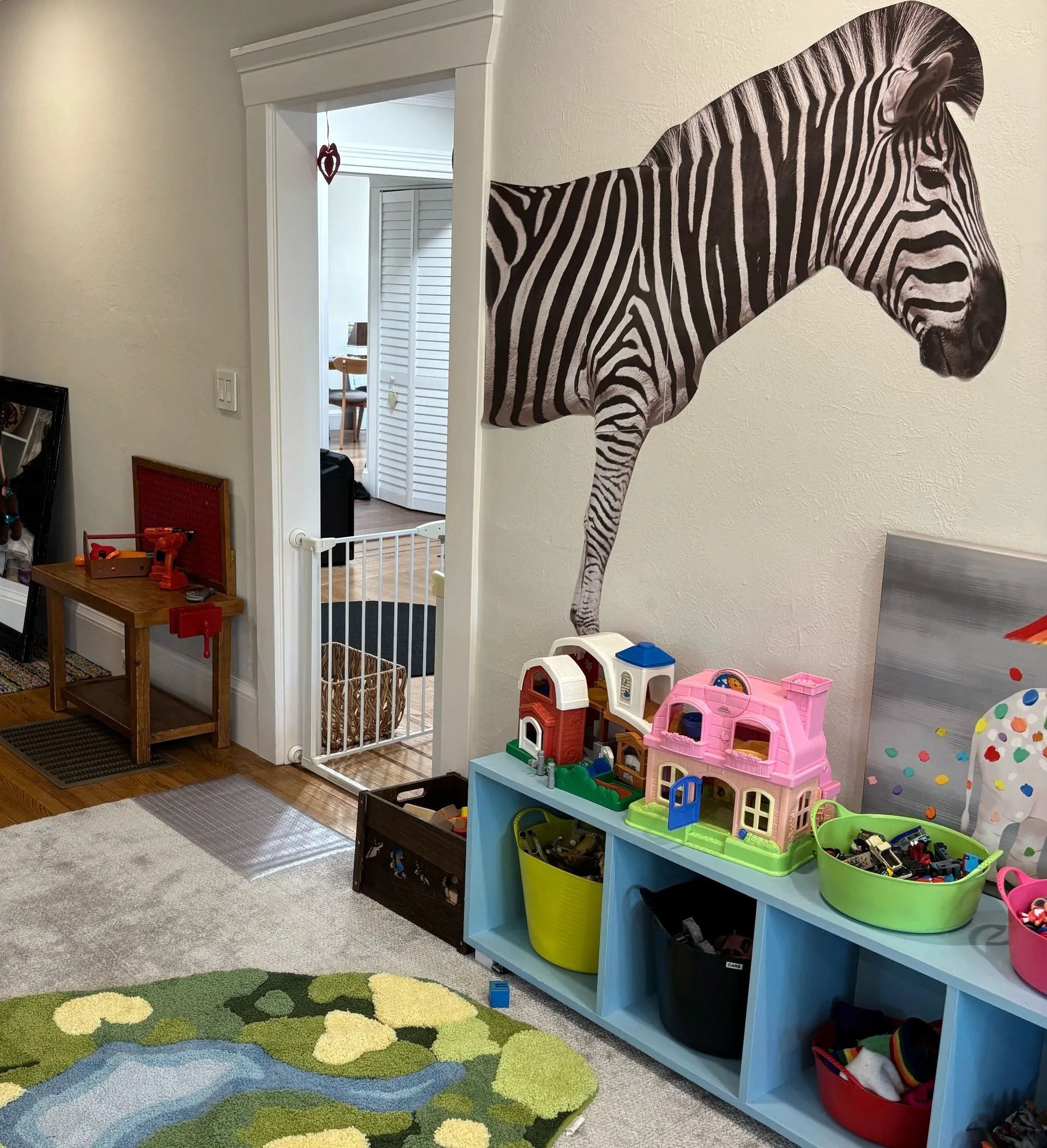 Kids’ playroom with zebra wall mural, toy shelf, mirror, and play rug