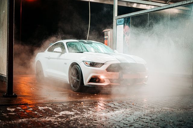 A white mustang is being washed in a car wash.