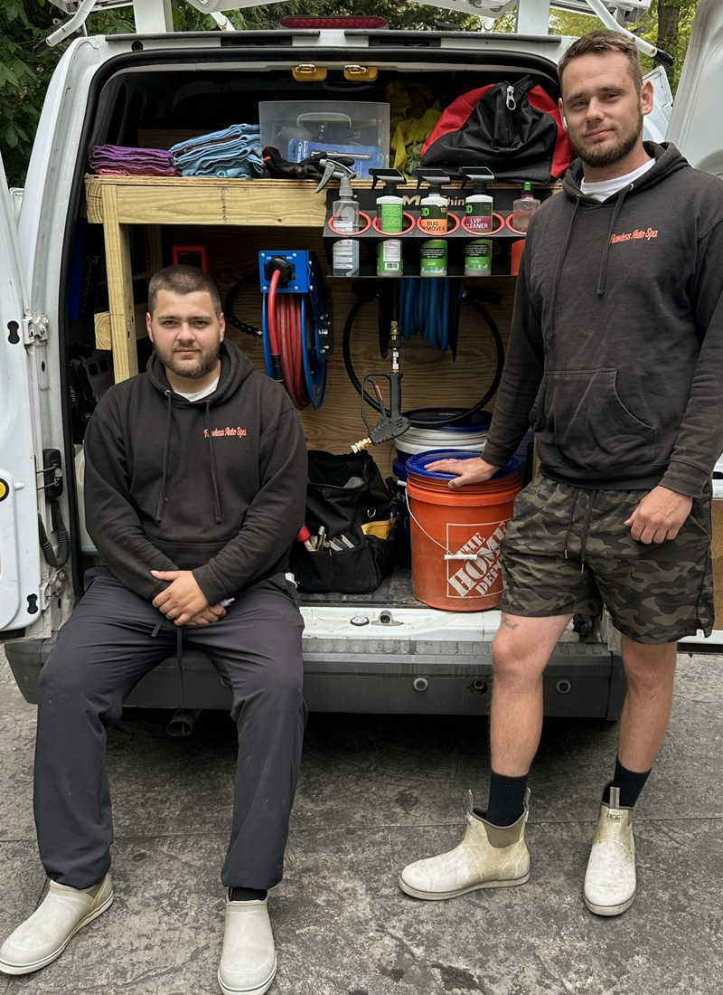 Two men are sitting in the back of a van. Auto detailing employees. 