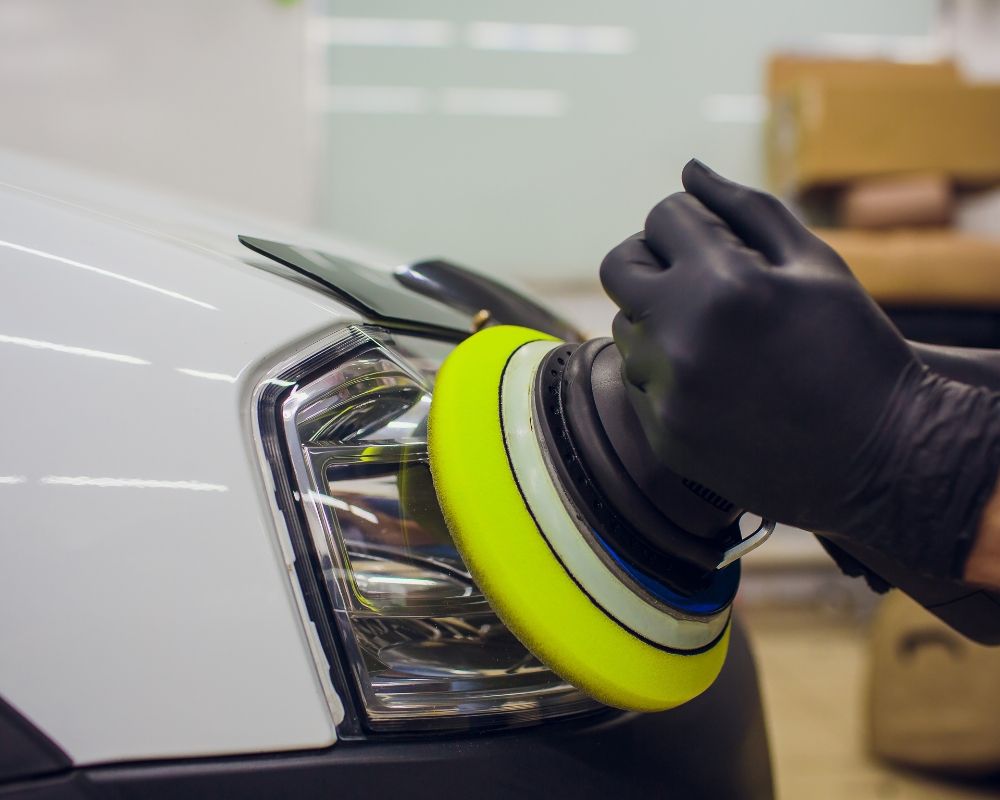 A person is polishing a white car with a yellow polisher.