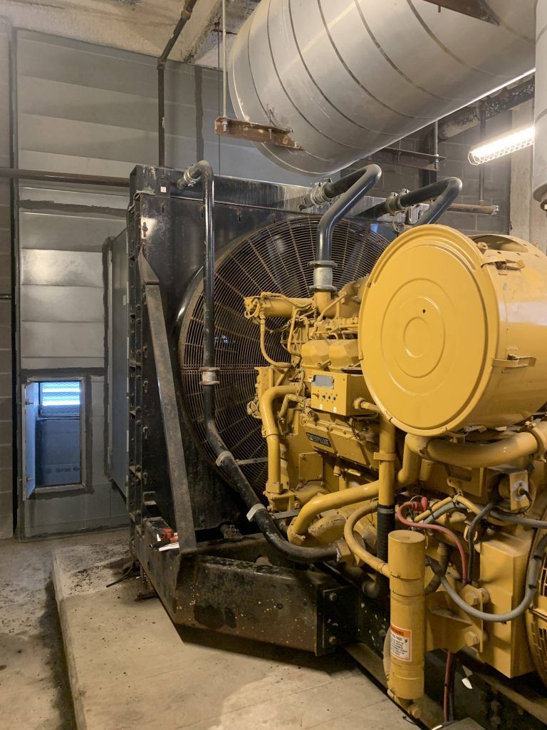 Large yellow Caterpillar generator in a building, with a large fan.