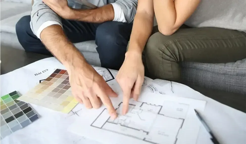 A man and a woman are sitting on a couch looking at a floor plan.