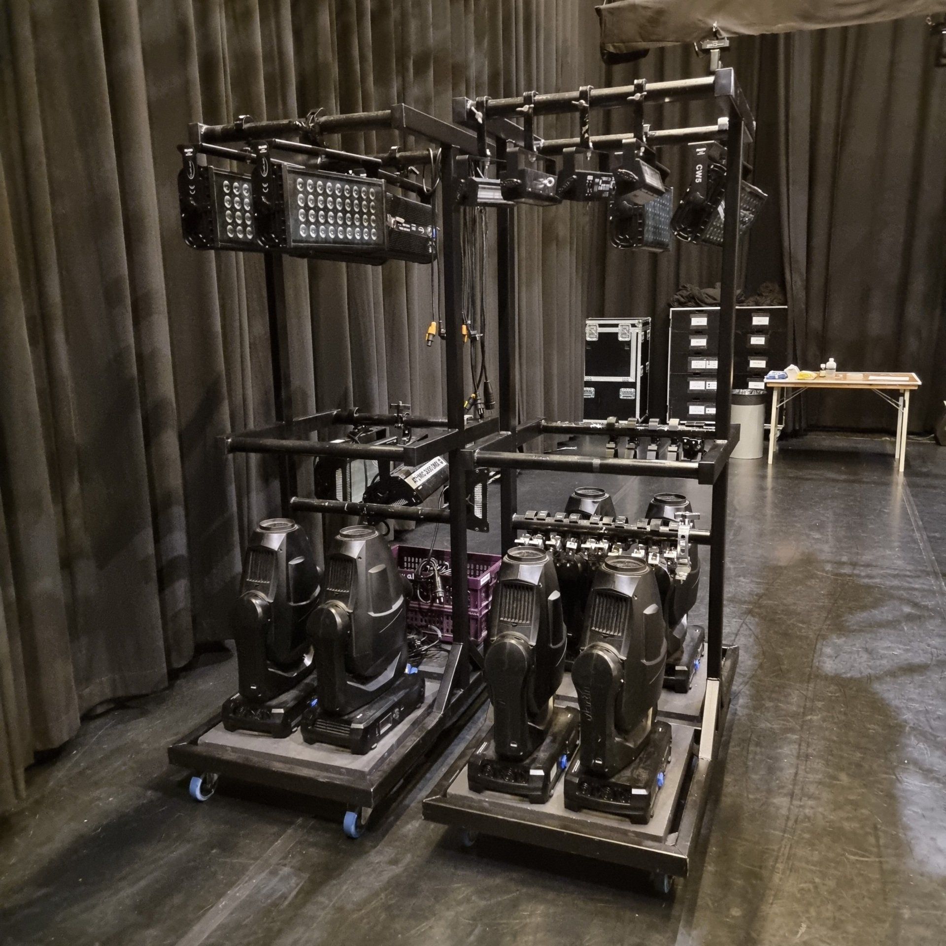 Twee metalen karren bevatten professionele podiumverlichtingsapparatuur, waaronder moving head-armaturen en rechthoekige ledpanelen.