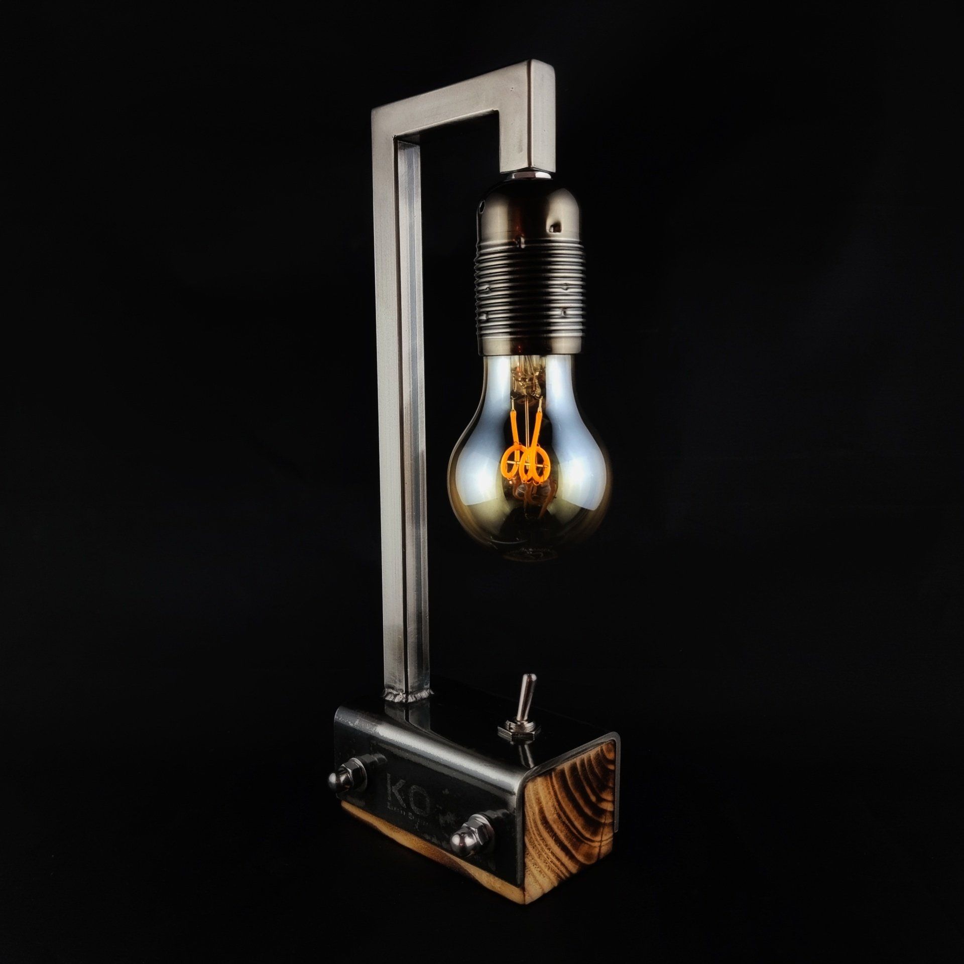 Bureaulamp in industriële stijl met een vintage Edison-lamp, metalen frame en houten voet, geplaatst tegen een zwarte achtergrond.
