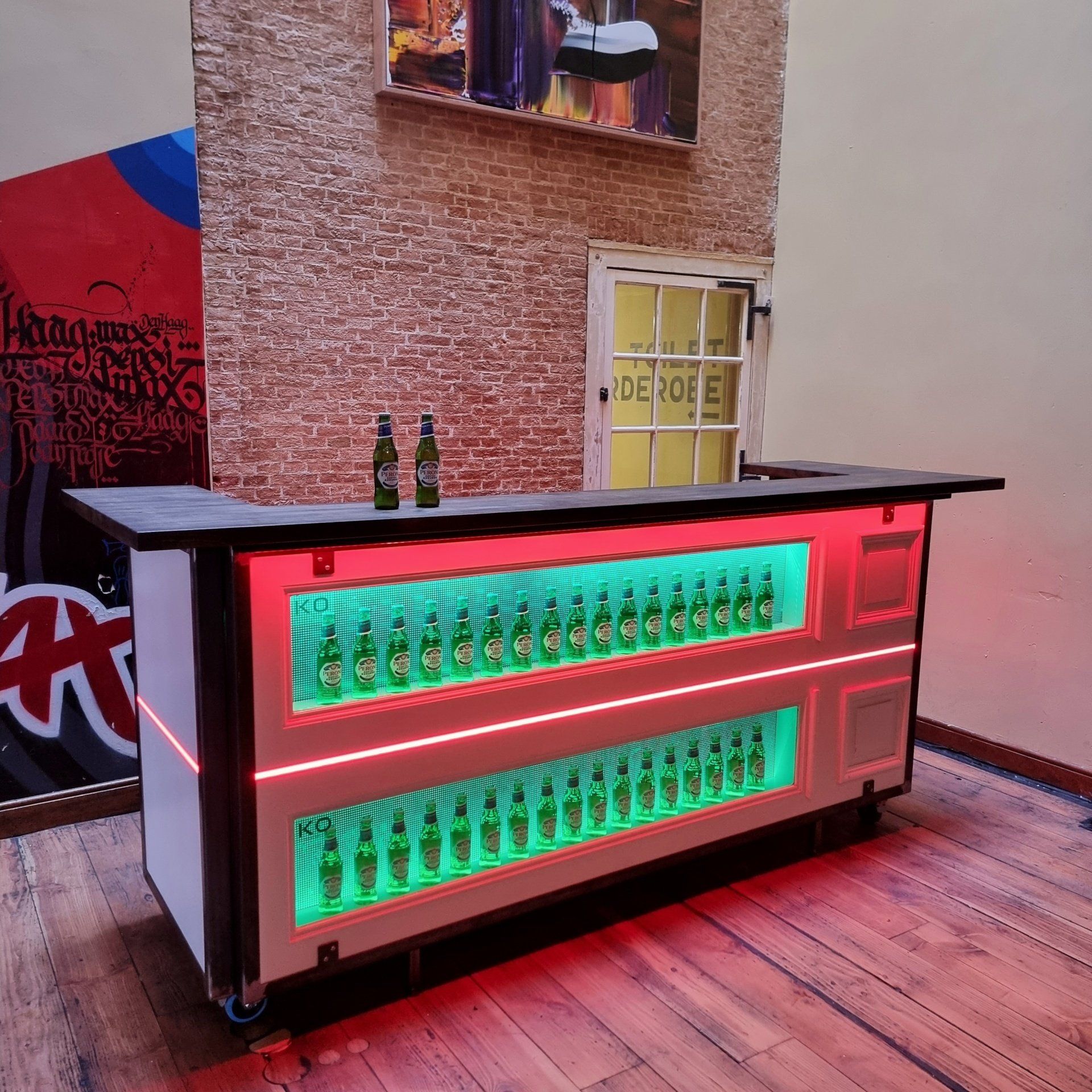 Een mobiele bar met neon-groene lichtdisplays van glazen flessen, geaccentueerd door rode ledstrips, op een houten vloer.
