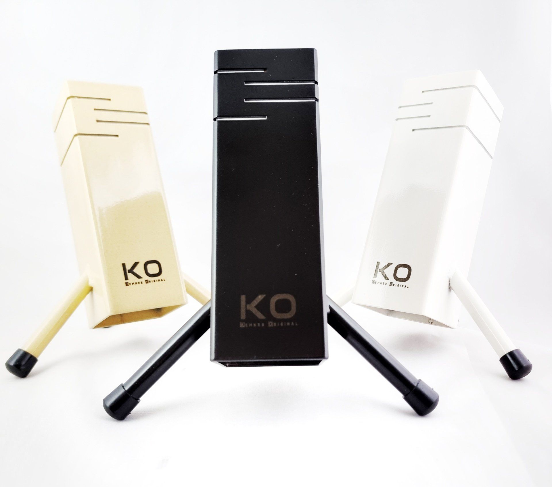 Drie slanke, rechthoekige KO-apparaten op standaards in zwart, wit en beige, geplaatst tegen een witte achtergrond.