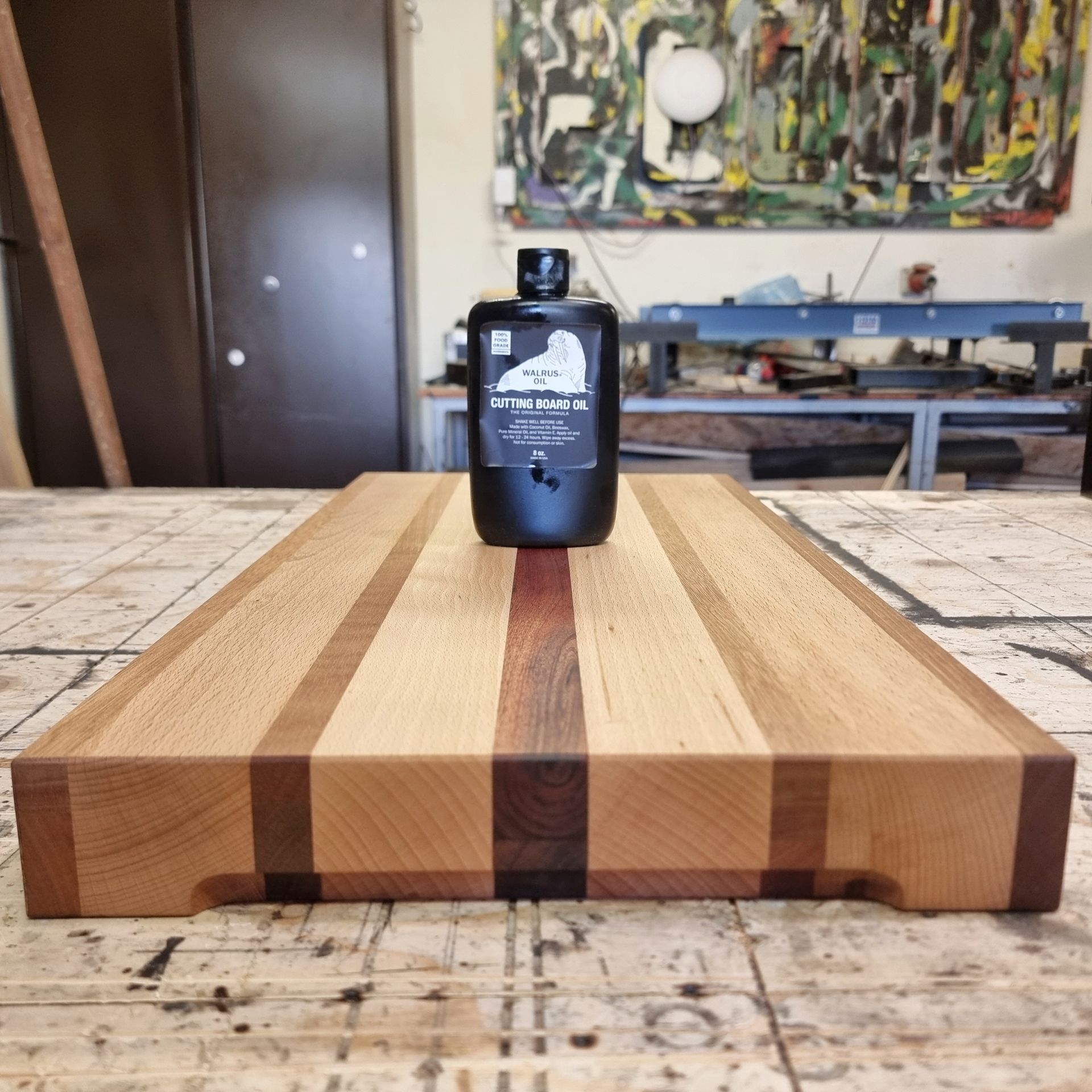 Een houten snijplank met afwisselend donkere en lichte houten stroken, met daarop een fles minerale olie in een werkplaats.