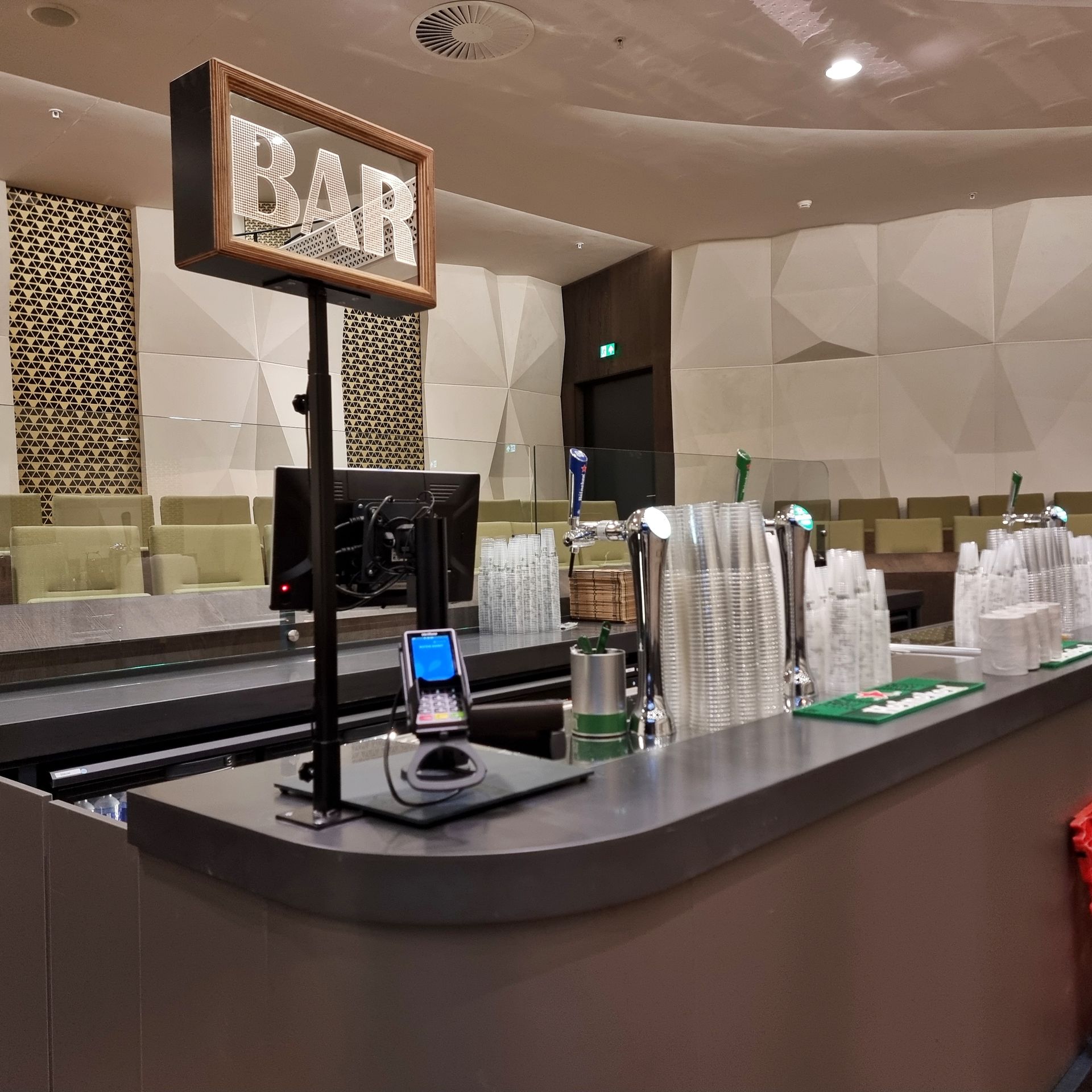 Een moderne binnenbar met een uithangbord boven de toonbank, biertaps en een betaalterminal.