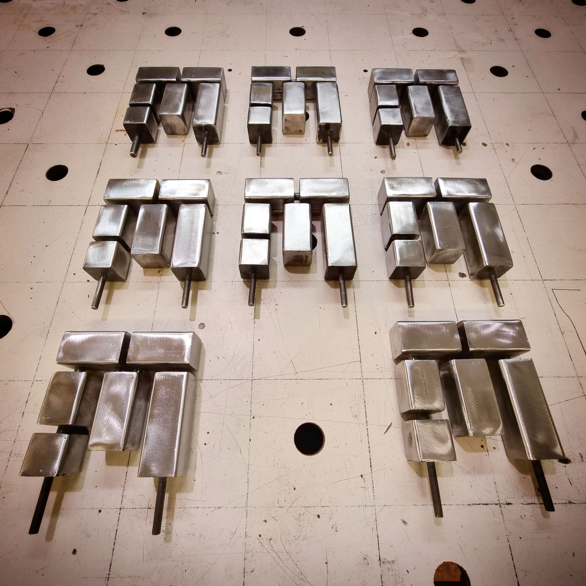 Acht metalen, U-vormige industriële componenten, gerangschikt op een rasterwerktafel met ronde montagegaten.