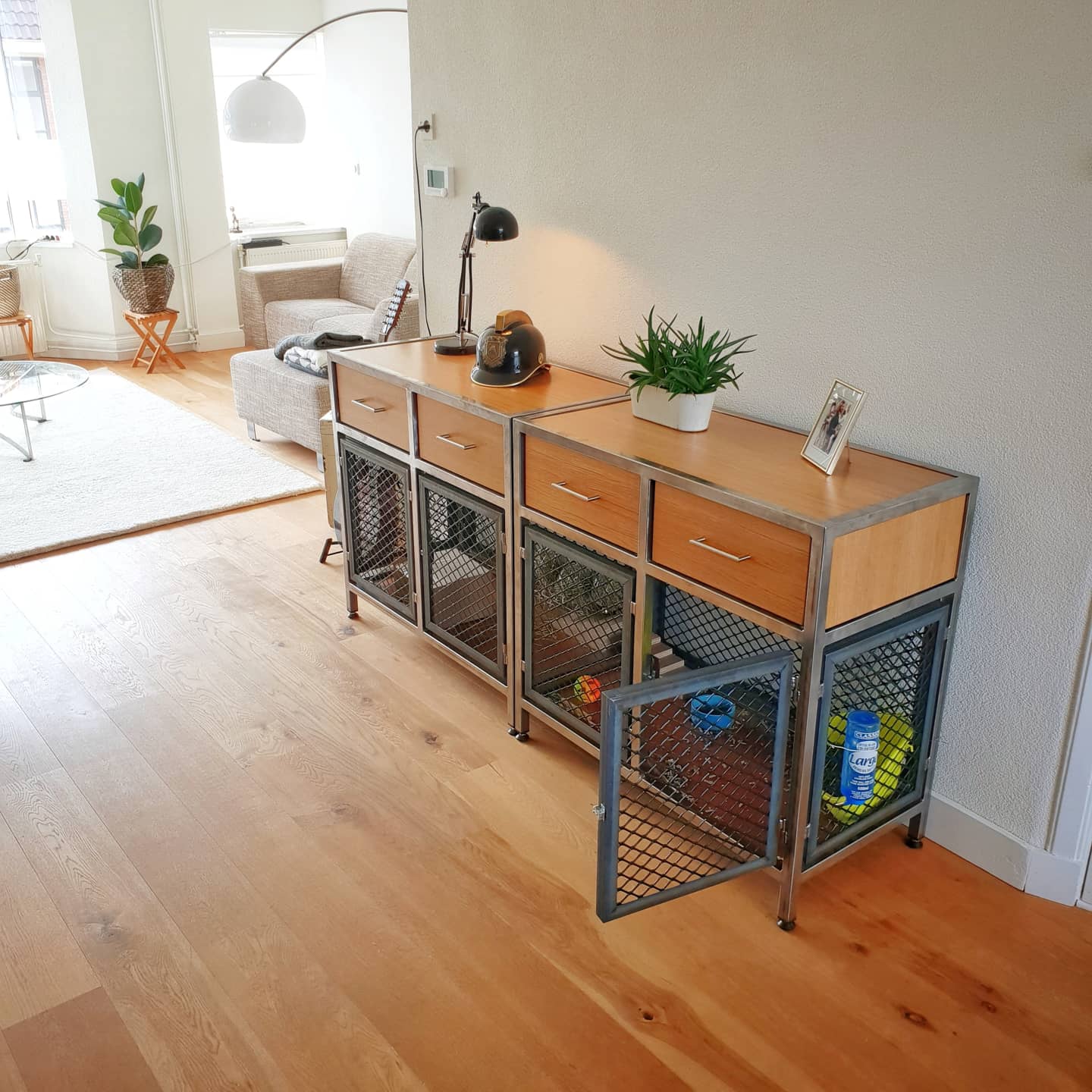 In een lichte woonkamer staan ​​twee houten kasten in industriële stijl met deuren van metalen gaas, die op een lichte houten vloer staan.