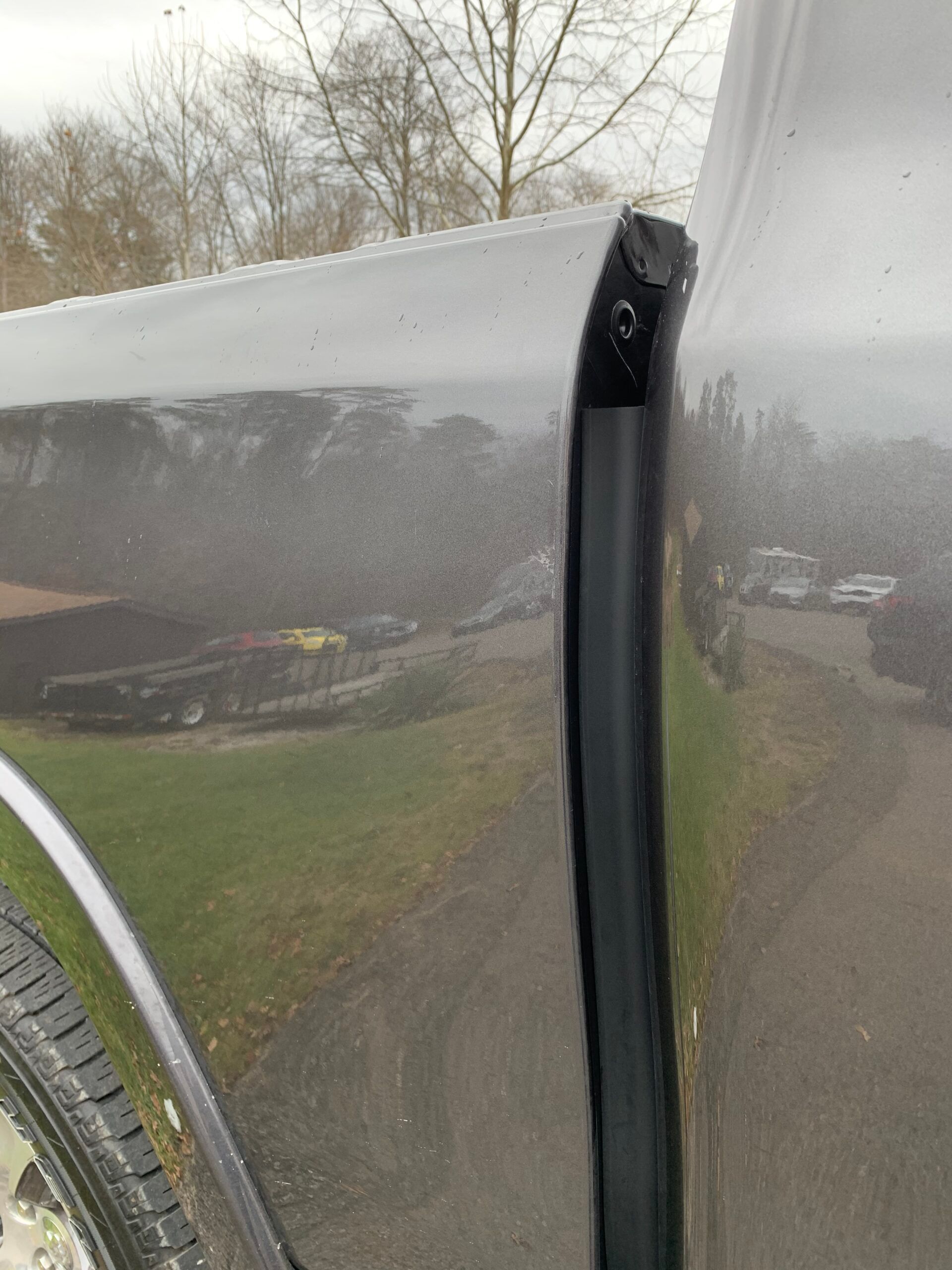 Close-up of a black car door seam with a white panel edge and snowy outdoor reflections
