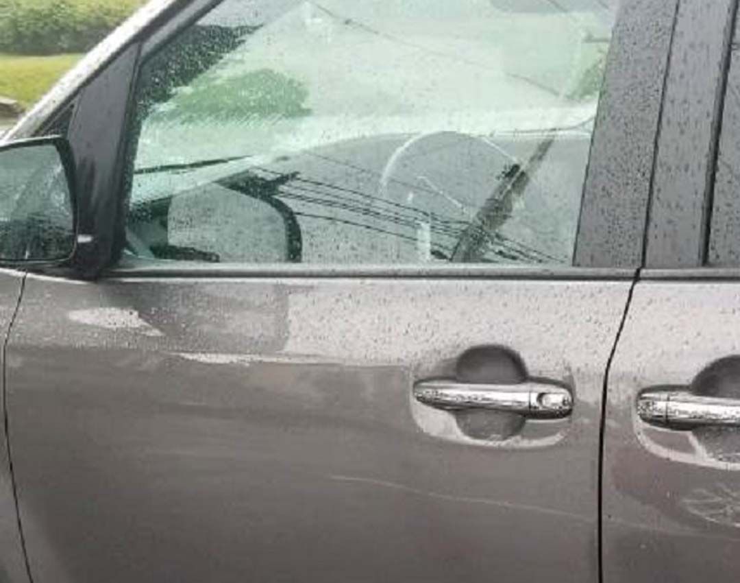 Close-up of a gray car door and window with raindrops on the glass and body.