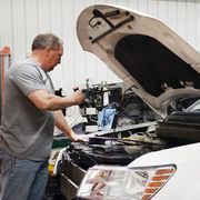 Man working on a white car with the hood open in an auto repair shop