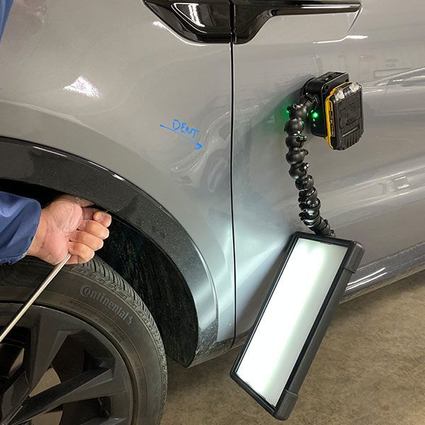 Technician measuring car body dent near rear wheel with inspection light and gauge
