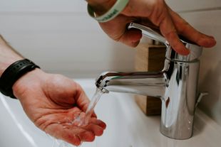 Person washing hands under a chrome faucet in a white sink; water running.