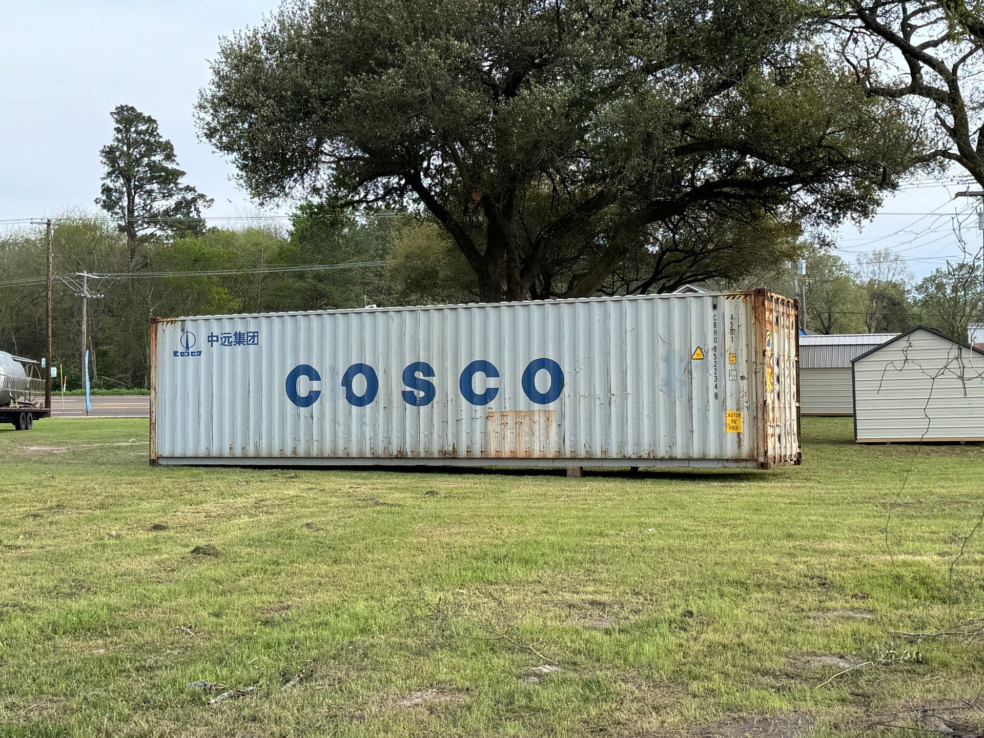 White COSCO shipping container in a grassy field with trees in the background