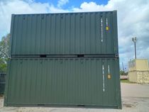 Green shipping container, doors open, on a concrete surface, outdoors.