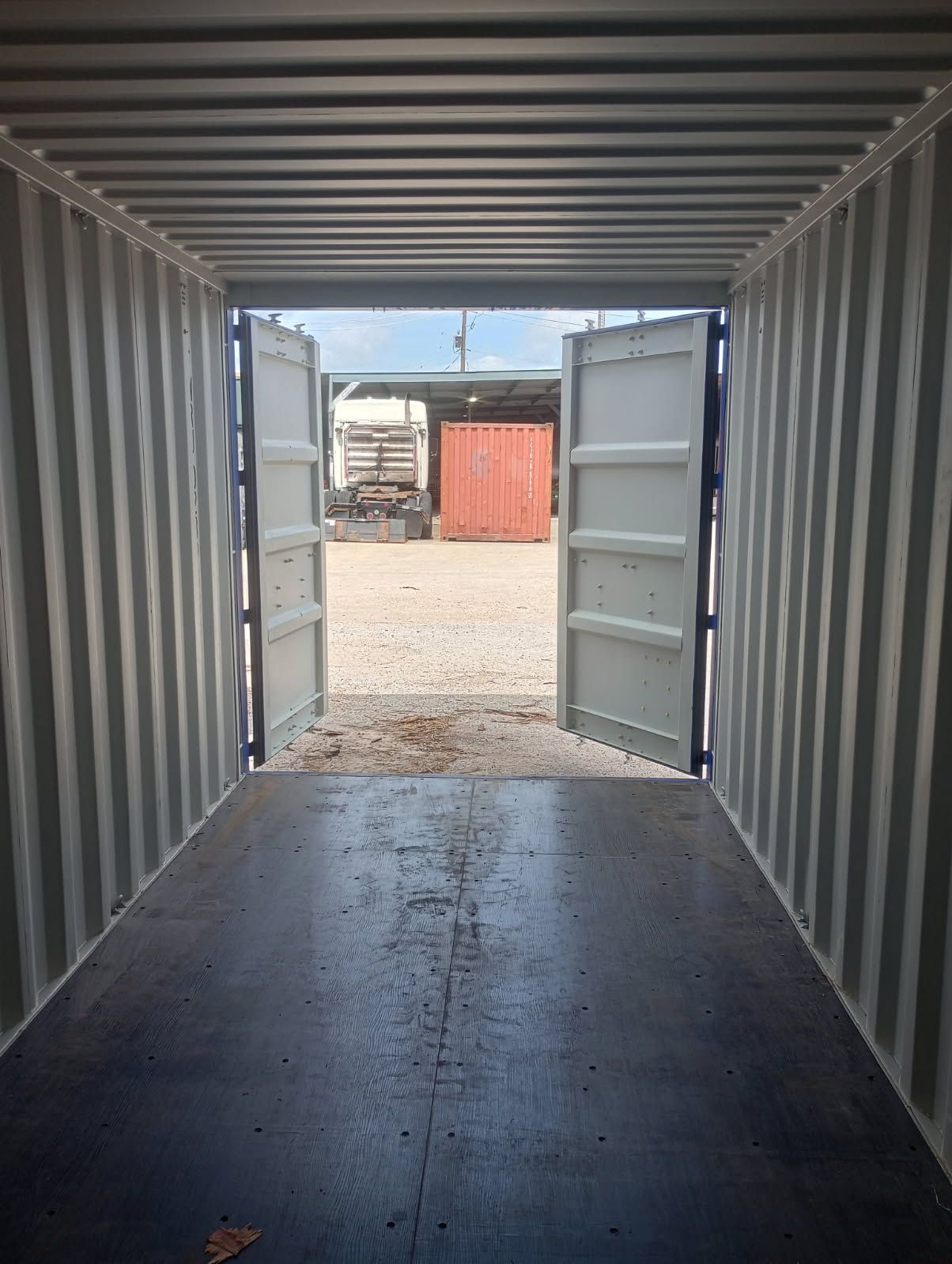 Stacked shipping containers of various colors, on a concrete surface against a blue sky.