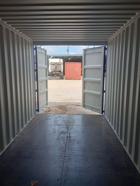 Shipping container in a field with green grass, mountains, and a cloudy sky.