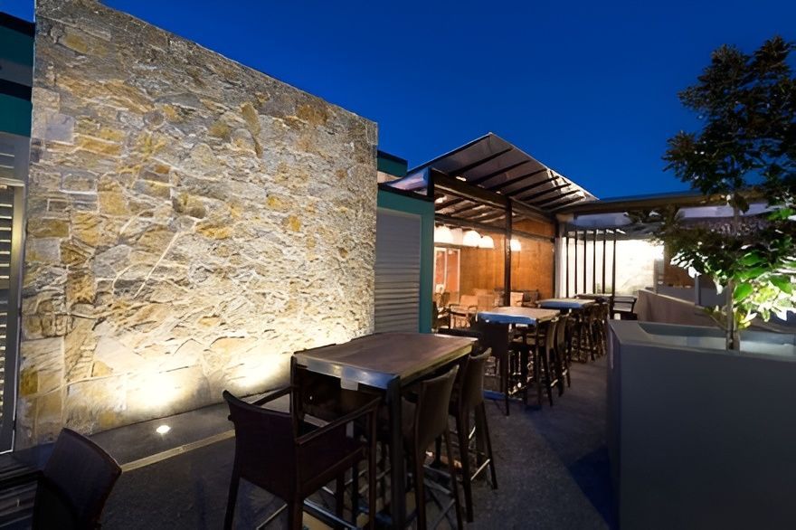 Outdoor Bar Area at Night With Stone Wall and Tables With Chairs — Darren Gray Cad Services In Upper Corindi, NSW