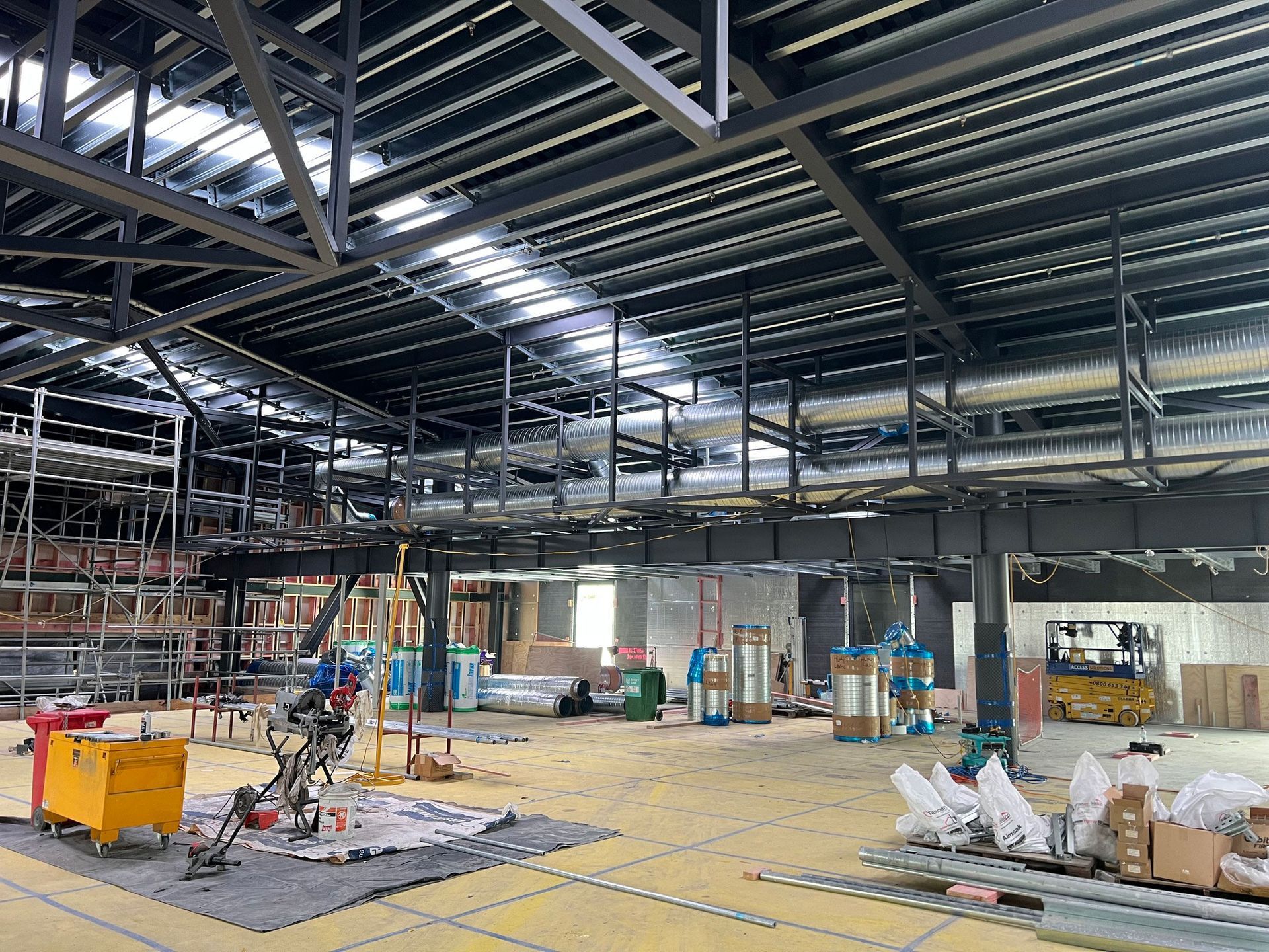 Interior of a large building under construction. Metal roof, exposed ductwork, construction materials and machinery.