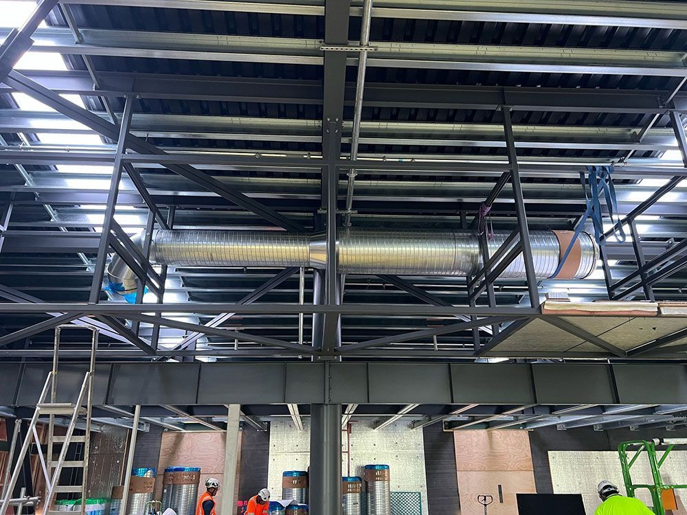 Construction site interior with exposed metal framing, ductwork, and scaffolding.