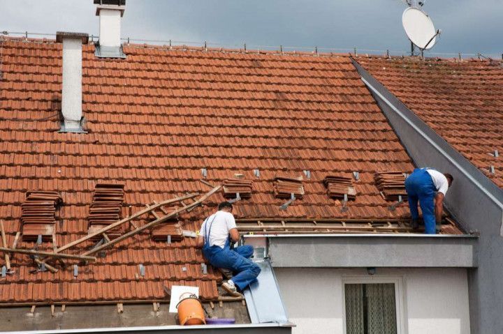 Roofers working on a red tile roof, removing and replacing tiles.