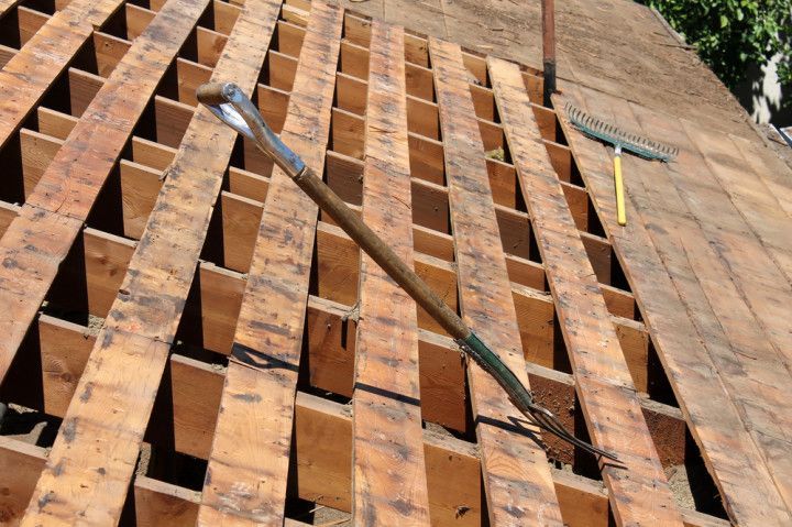 Rooftop with exposed wooden support beams; a tool and rake are resting on the beams.