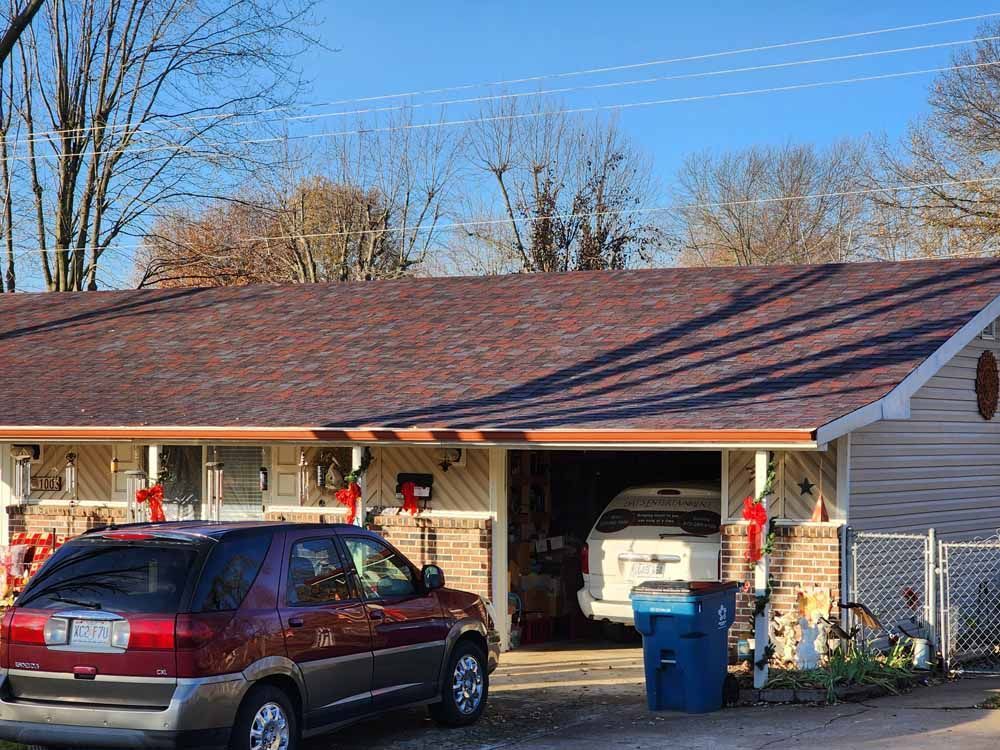 A house with a red roof, a car parked in front, and a car inside an open garage.