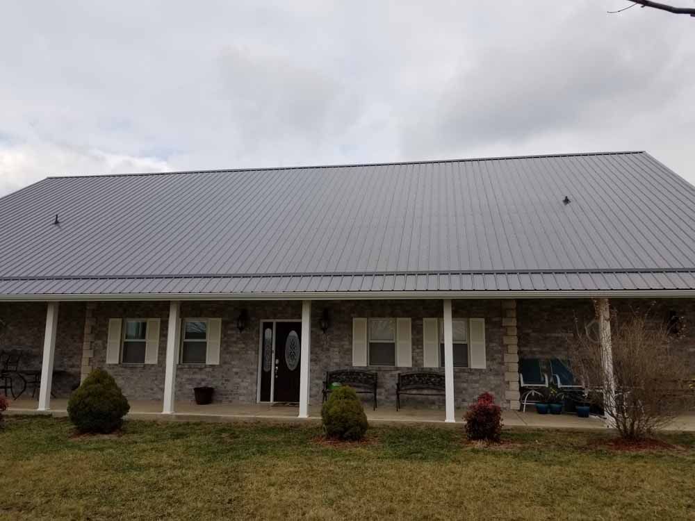 Gray metal-roofed house with a covered porch and white columns; cloudy sky.