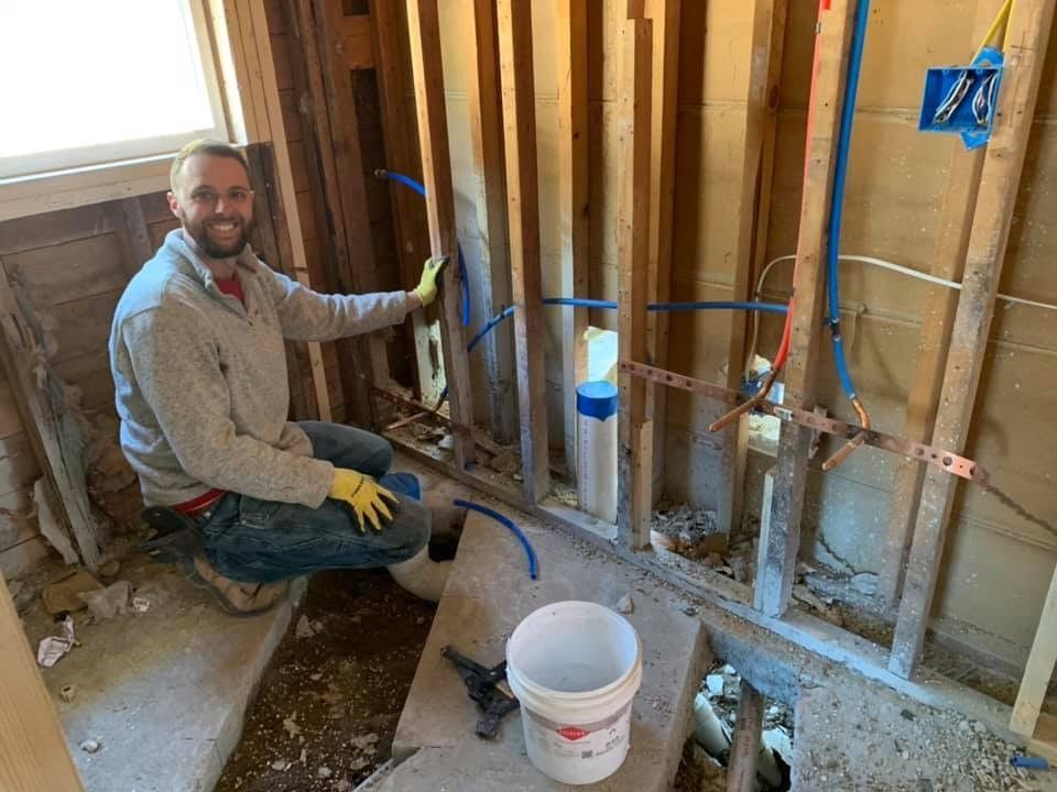 A man is kneeling down in a bathroom while working on pipes.