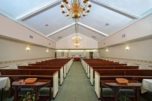 Empty church pews facing a central aisle under chandeliers in a bright sanctuary