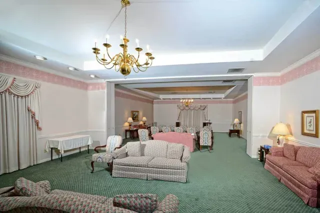 Elegant hotel-style living room with green carpet, pink sofas, chandeliers, and draped windows
